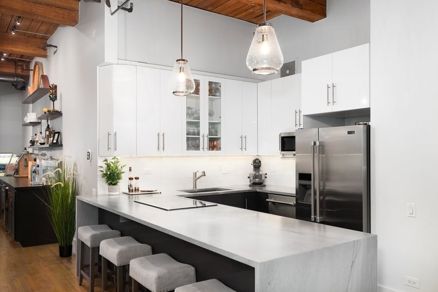 A Beautiful Luxury Kitchen With White Cabinets, Maytag Refrigerator, Stainless Steel Appliances, A Grey Waterfall Granite Countertop, And An Exposed Beam Ceiling.