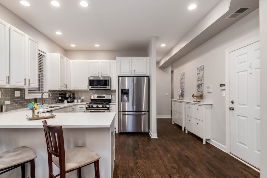 A White Kitchen With Black Counter Top And Stainless Steel Samsung Appliances.