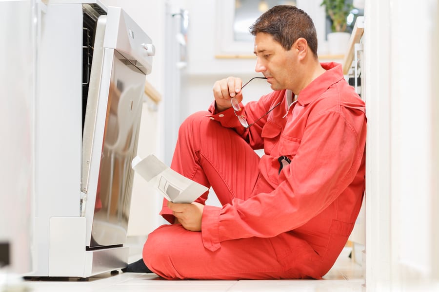 Handy Man Reading The Instruction Manual In Front Of The Dishwasher In The Kitchen