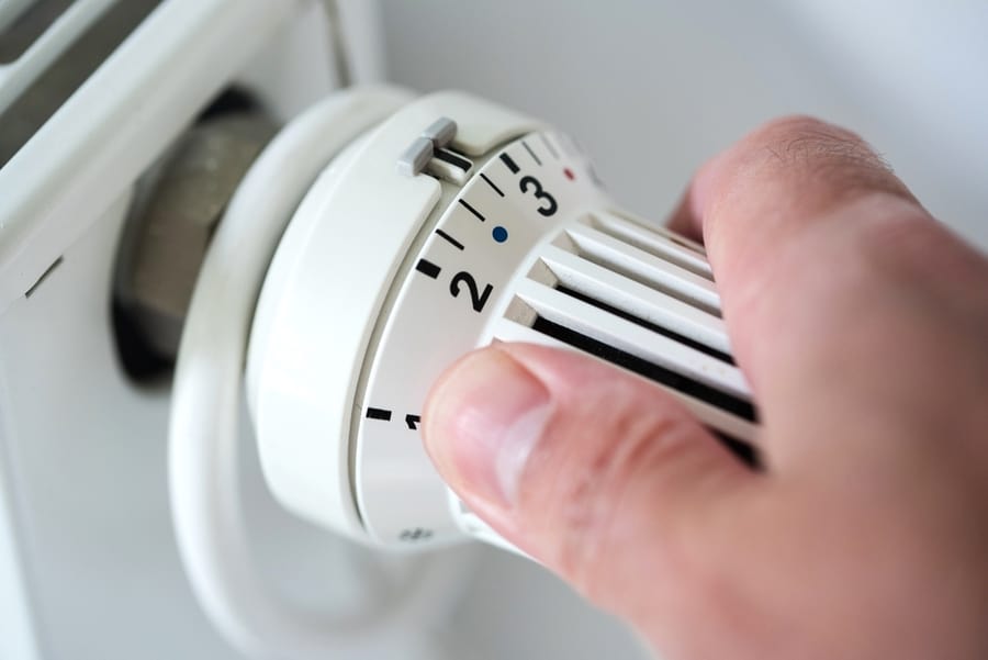 Person Adjusting Thermostat On Radiator To Lower Temperature