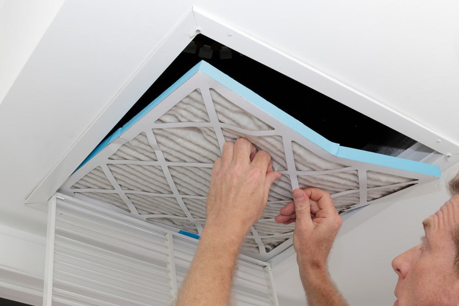 Person Removing An Old Dirty Air Filter From A Ceiling Intake Vent