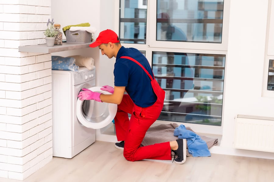 Plumber In Overalls With Tools Is Repairing A Washing Machine In The House