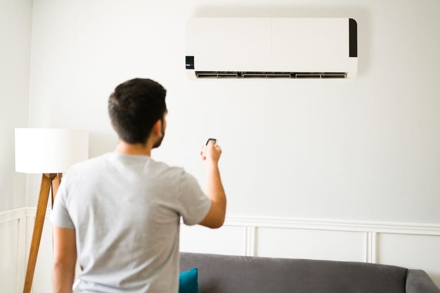 Rear View Of A Young Man Using The Remote To Turn Off The Air Conditioning In The Living Room