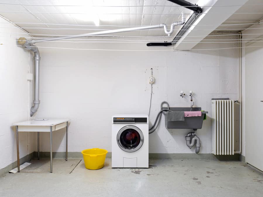 Shared Apartment Building Laundry Room With Washing Machine In Used Wash Sink And Piping Wide Angle View