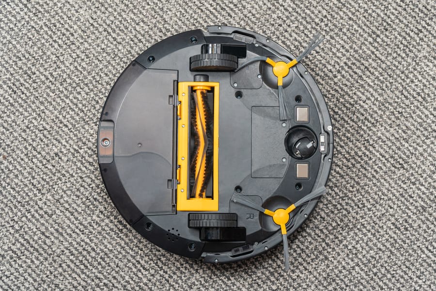 Upside Down Robot Vacuum Cleaner Lying On A Carpet For Cleaning Brushes And A Waste Bin