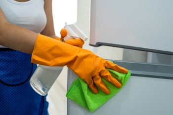 Beautiful And Happy Housekeeper Cleaning Refrigerator Doors With Rag