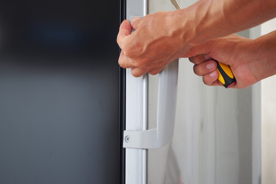 Closeup Of A Man Sets The Handles To A New Refrigerator With A Screwdriver.