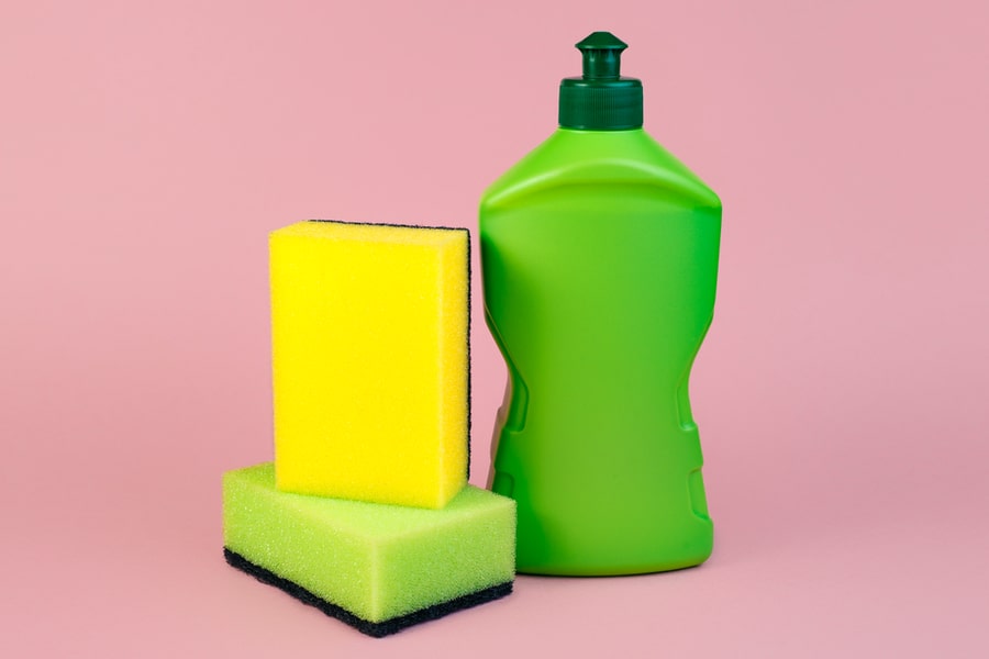 Green Bottle Of Dishwashing Detergent And Sponges On Pink Background.