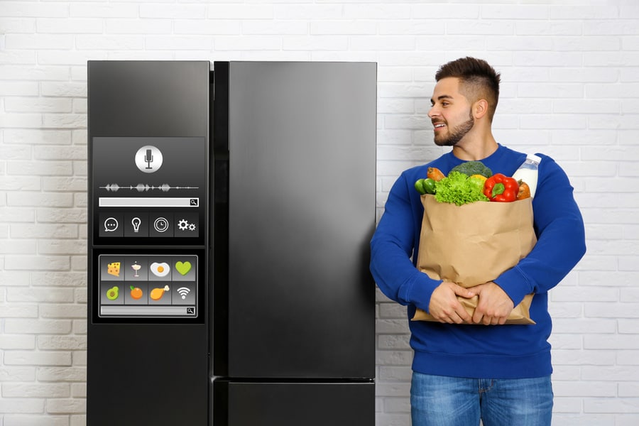 Man Holding The Groceries While Using The Voice Control Feature Of The Smart Fridge