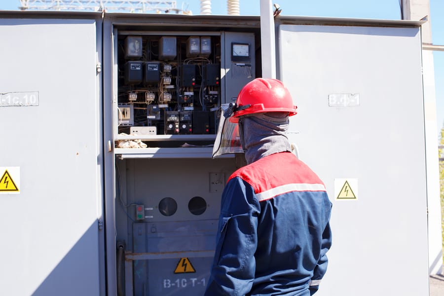 The Duty Electrician Of Power Transformer Substation In Overalls And A Protective Helmet Makes Expeditious Switchings