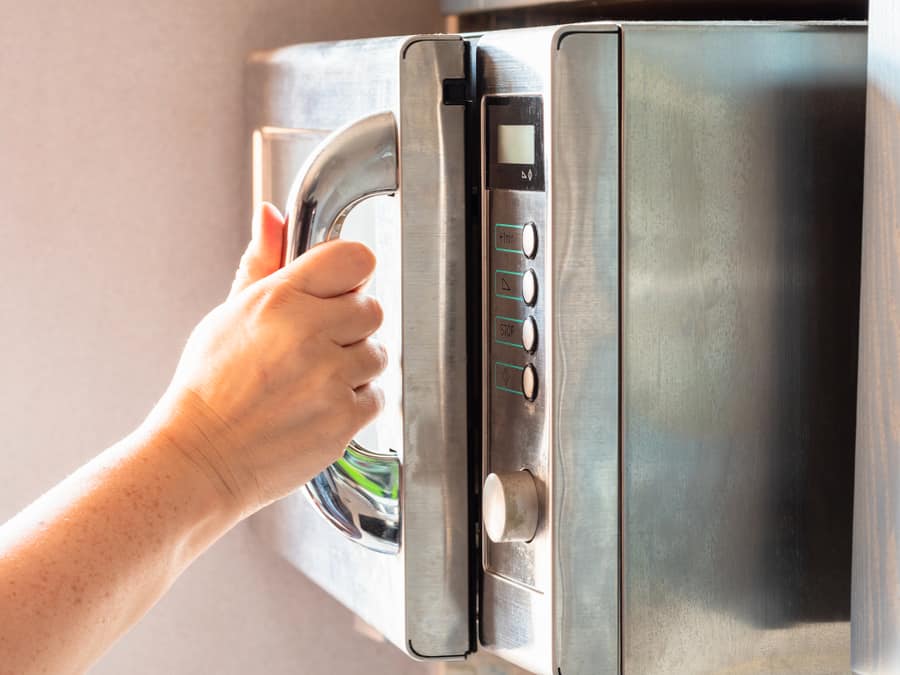 The Illuminated By Sun Hand Opens An Old Steel Microwave Oven At Home