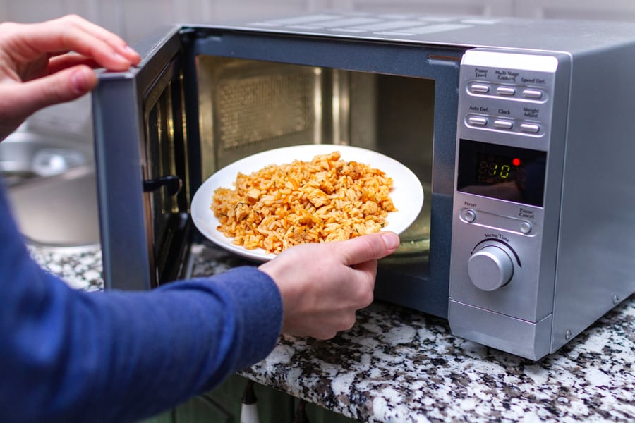 Woman Reheating Food Using Microwave Oven