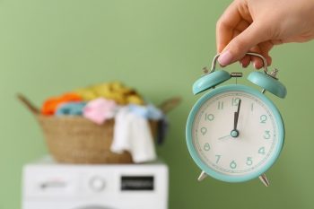 Woman With Alarm Clock On Bathroom Interior Background, Closeup