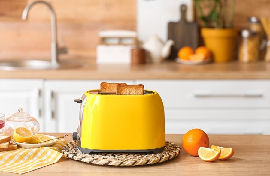 Yellow Toaster With Bread And Orange Slices On Table In Kitchen