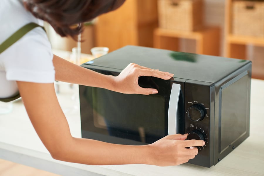 Young Woman Setting Time On Microwave