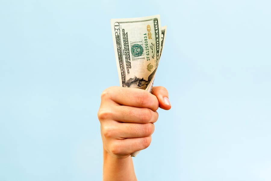 A Hand Holding A Handful Of Twenty Us Dollars, On Blue Background.