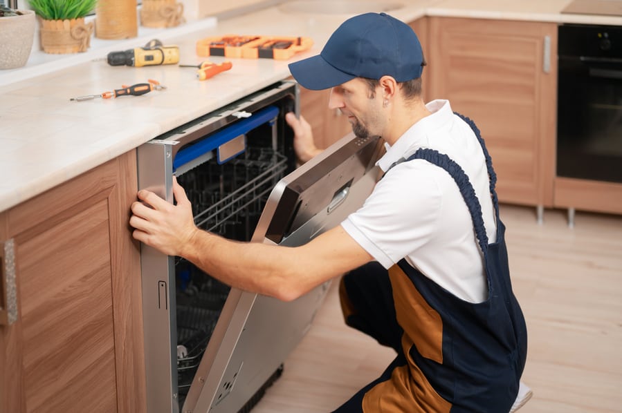 A Man Or Service Worker In Special Clothing Installs, Disassembles Or Performs Maintenance Of A Dishwasher Built Into The Kitchen Furniture.