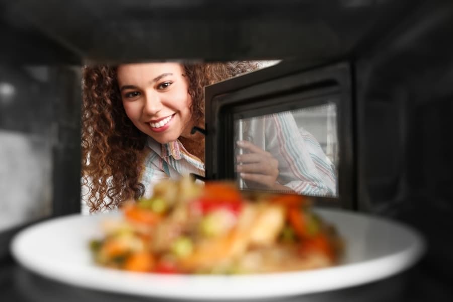 African-American Woman Heating Food In Microwave Oven