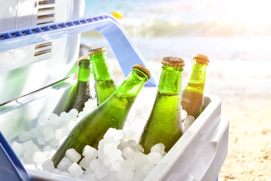 Bottles Of Beer Chilled On Ice In A Camping Fridge On A Beach On A Hot Day With Sunshine.