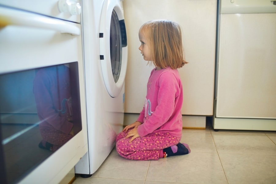 Child Sitting On The Floor Infront Of Balanced Washing Machine