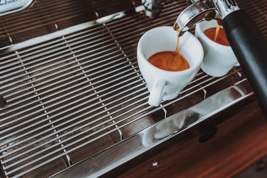 Close Up Of Coffee Machine Drip Tray And Two White Cups Standing On It While Coffee Pouring Into Them