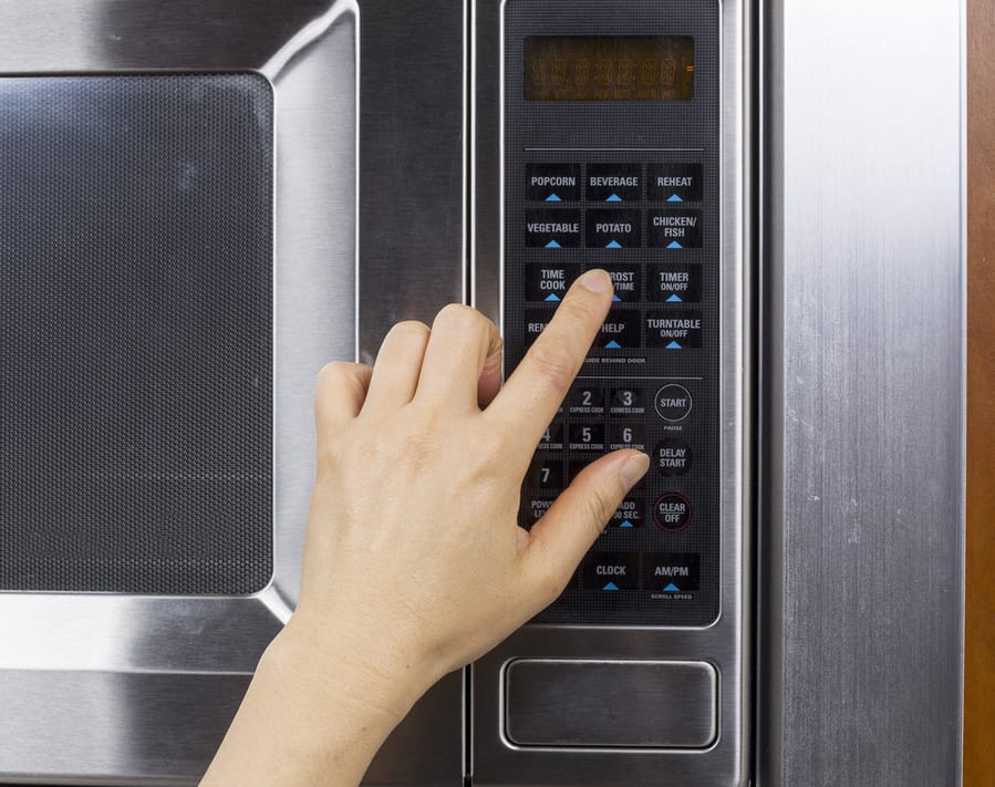 Hand Preparing To Activate Defrost Mode On Microwave Oven