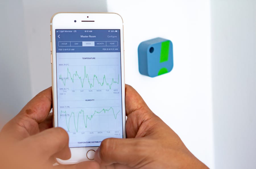 Man Monitoring Home Humidity Levels And Temperature With A Hygrometer Sensor And An App With Graphs On A Mobile Phone
