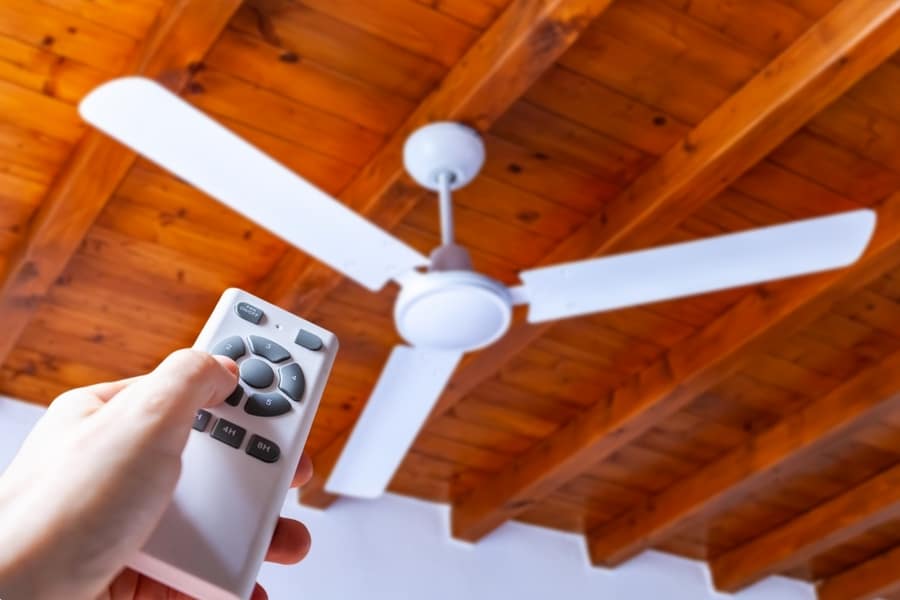 Man Uses A Remote Control To Turn On A White Ceiling Fan Mounted