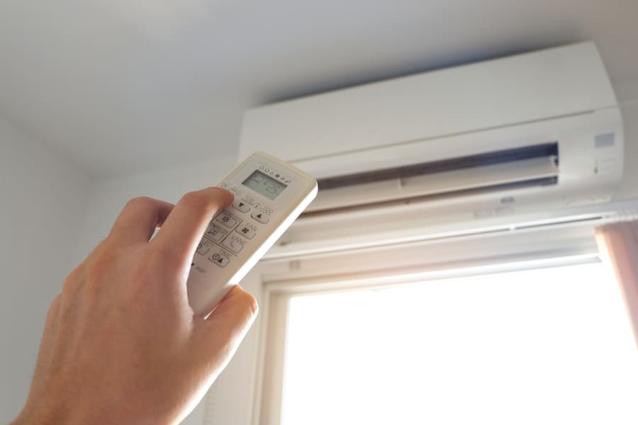 Man's Hand Using Remote Control Open The Air Conditioner Is Cooled To 25 Degrees Celsius In His Bedroom.