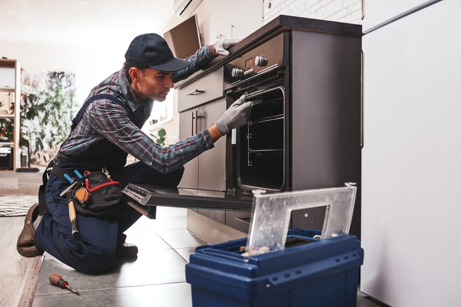 Repairman Examining Oven With Screwdriver
