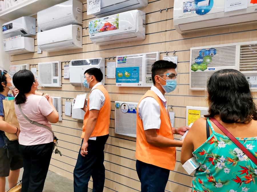 Sales Personnel In Face Masks And Shields Assist Customers At The Air Conditioning Section Of An Appliance Store.