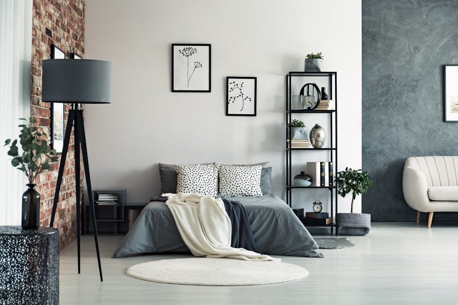 Vase On Metal Table And Grey Lamp In Spacious Bedroom With White Carpet And Gallery On Wall Above Bed.