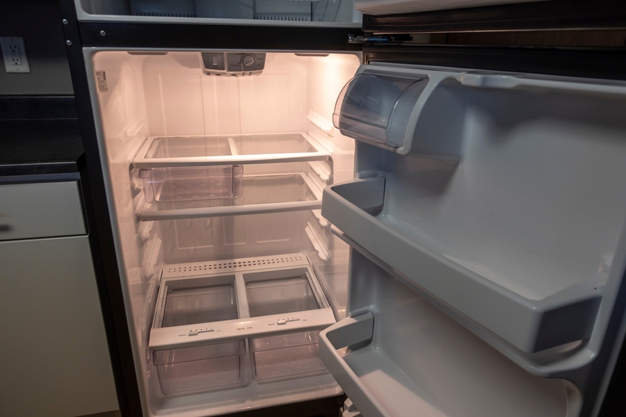 View Of A White, Empty Fridge With The Door Wide Open To See Several Shelves And Drawers Devoid Of Food
