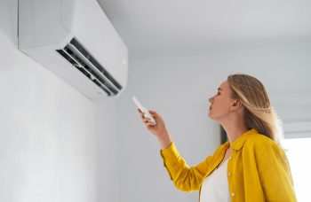 Woman Holding Remote Control Aimed At The Air Conditioner