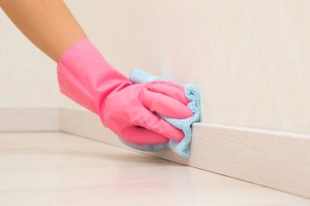 Young Adult Woman Hand In Pink Rubber Protective Glove Using Blue Dry Rag And Wiping Light Wooden Baseboard Surface