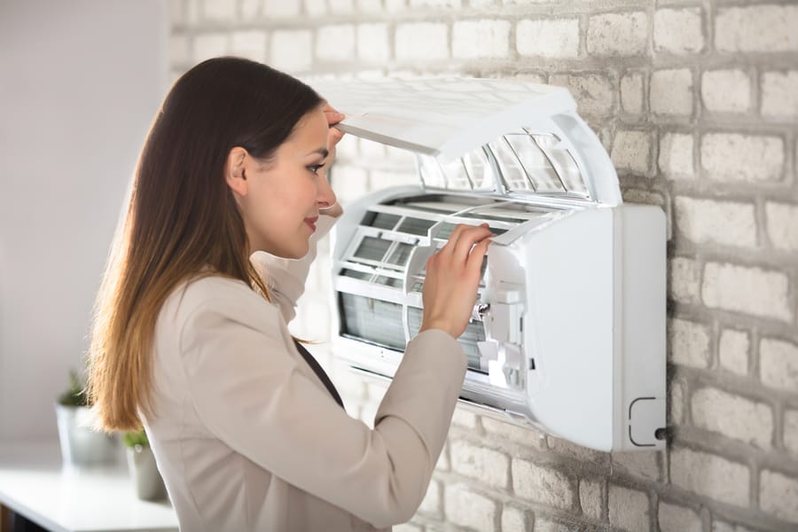 Young Woman Opening Air Conditioner Attached On Wall