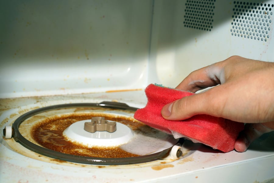 A Hand With A Sponge And Washing Foam Cleans The Microwave From Grease And Dirt