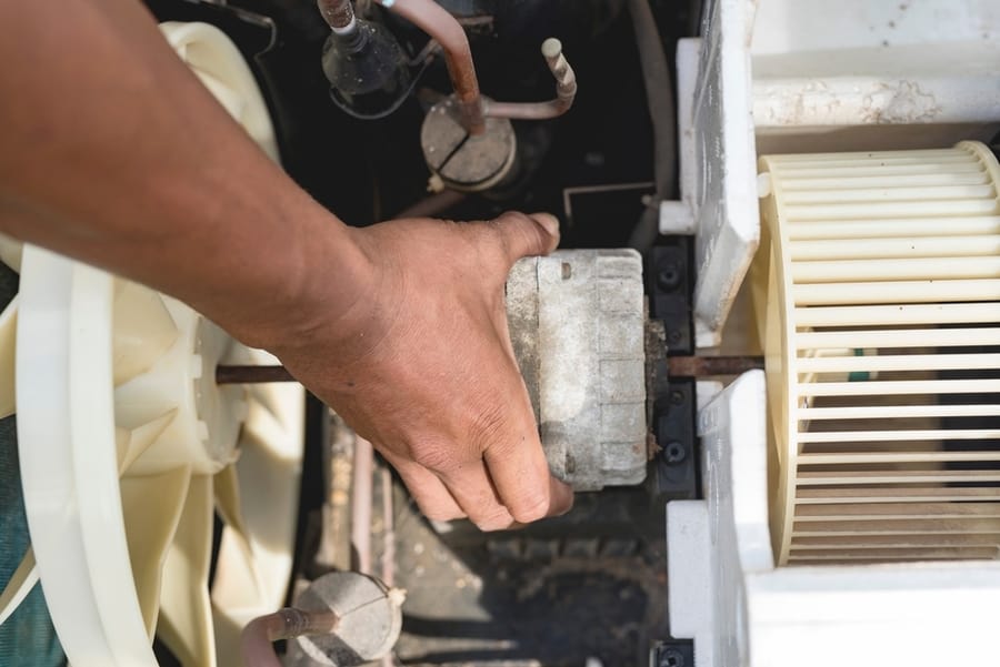 A Repairman Removes The Motor, Blower And Condenser Fan From A Window Type Ac