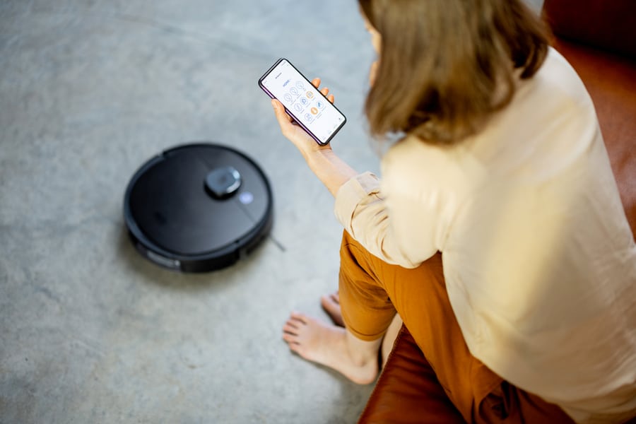 Black Robotic Vacuumer Is Cleaning The Floor While Pretty Woman Control The Robot