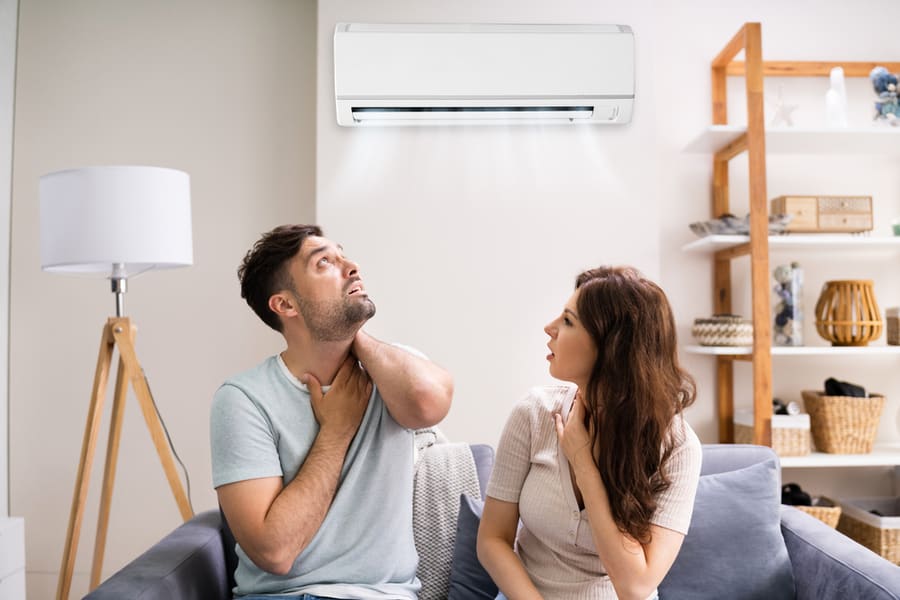 Couple Feeling Warm Air Coming From The Air Conditioner