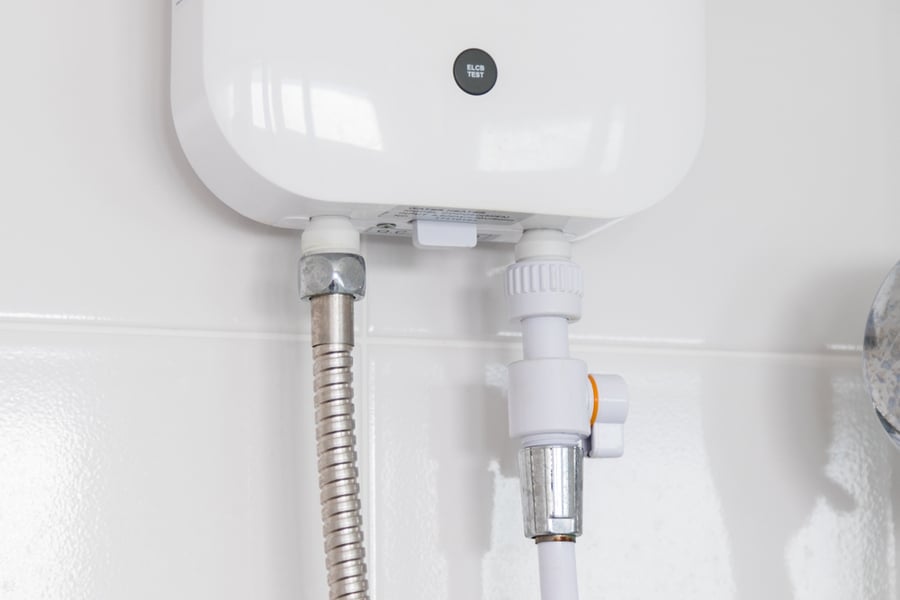 Instant Tankless Electric Water Heater Installed On White Tile Wall With Input And Output Pipe