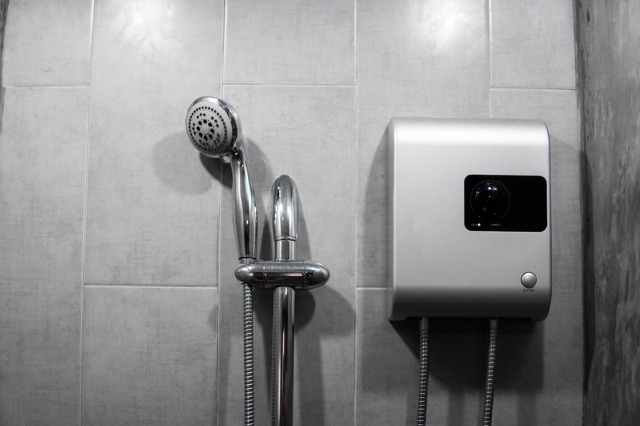 Instant Tankless Electric Water Heater Installed On Grey Tile Wall With Input And Output Pipe Outlet