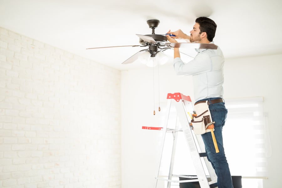 Male Electrician Stepping On A Ladder And Installing A Ceiling Fan