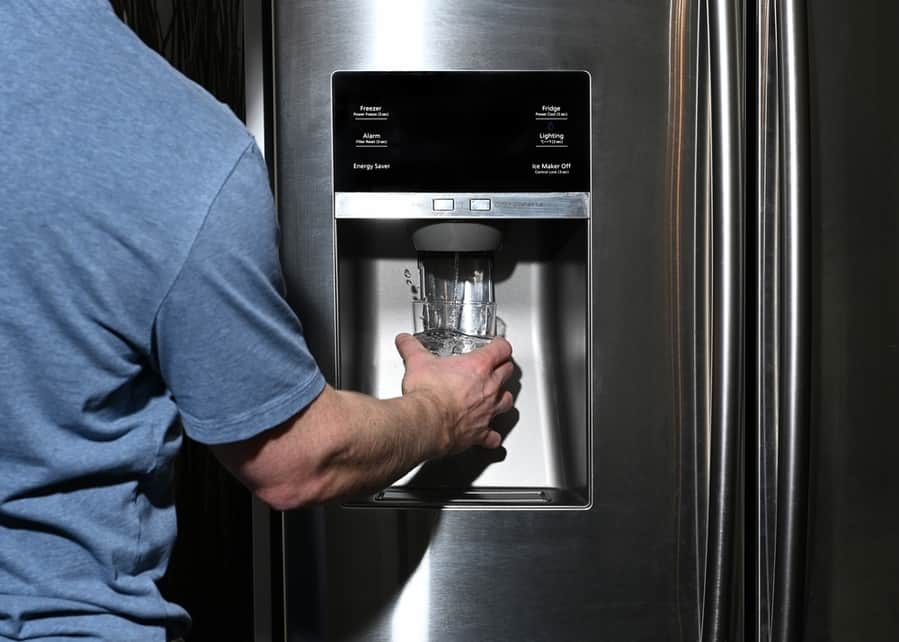 Male Right Hand Filling Glass With Water Splashing Out Of Dispenser Of Home Fridge