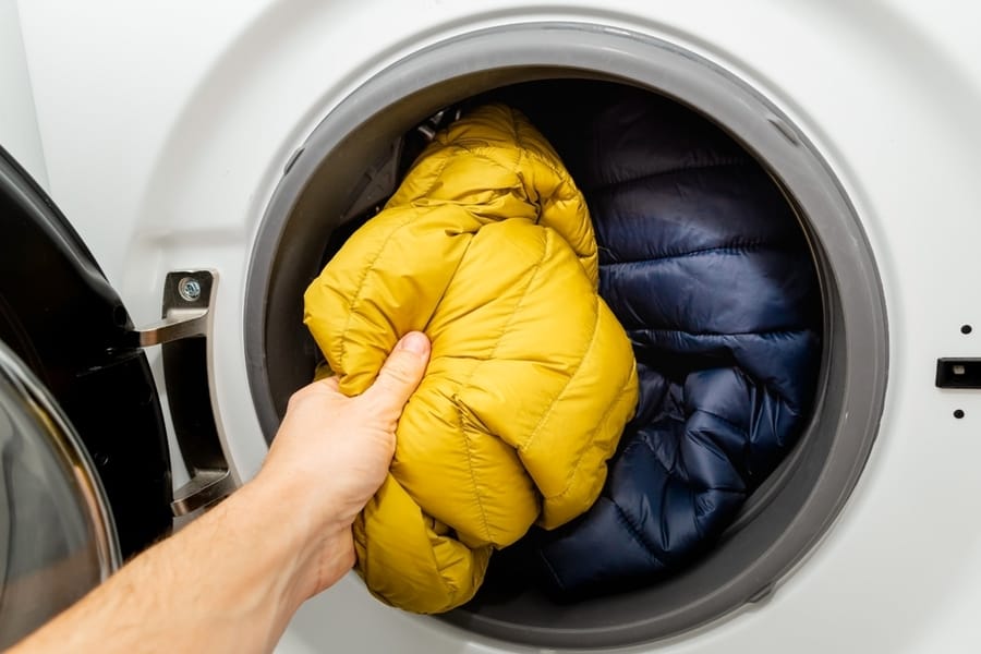 Putting Winter Jacket Into The Drum Of Open Washing Machine In Laundry Room.