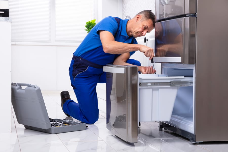 Serviceman Repairing Refrigerator With Toolbox In Kitchen