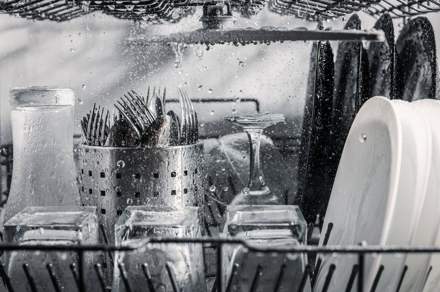 Transparent And Black And White Dishes As Well As Cutlery And Glasses Are Washed In The Dishwasher, Inside View, Drops And Splashes Of Water.