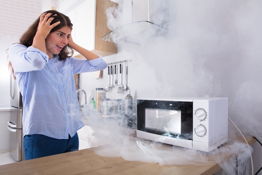 Unhappy Young Woman Looking At Smoke Emitting Through Microwave