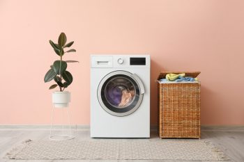 Washing Machine And Basket With Laundry Near Colored Wall