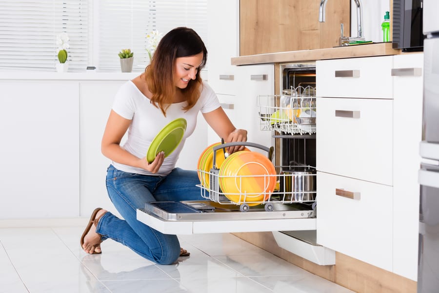 Woman Arranging Plates In Dishwasher At Home